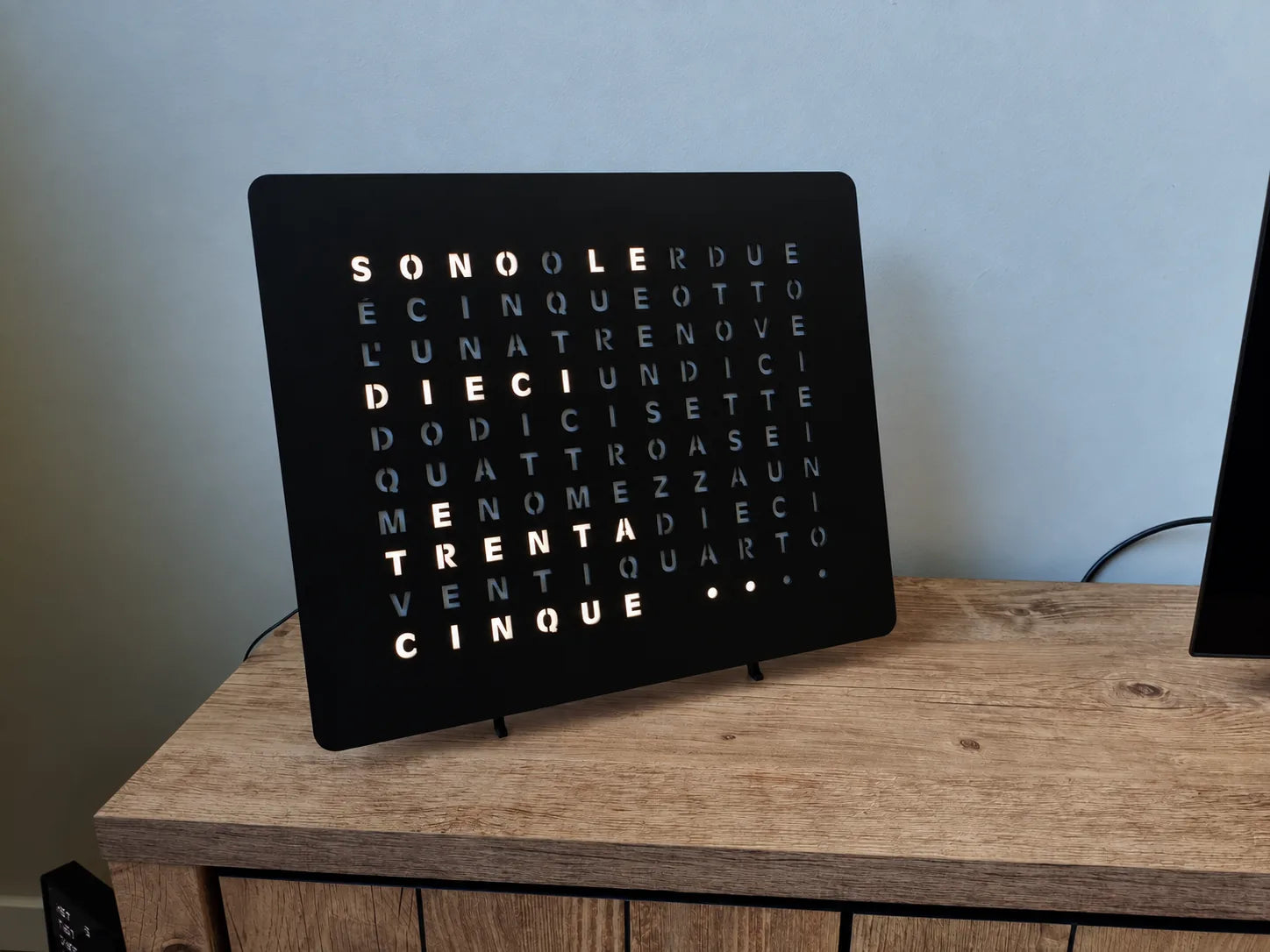 LumosClock edición italiana sobre un mueble de TV de madera con el soporte de mesa